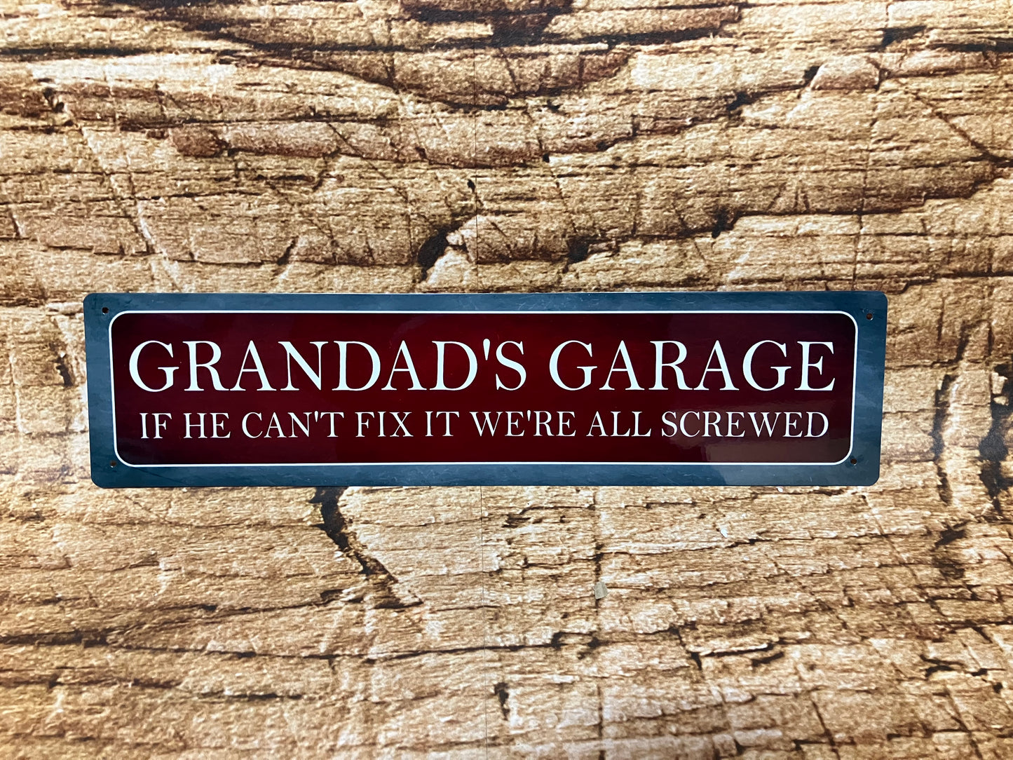 Humoristisch metalen bord met de tekst “GRANDAD'S GARAGE – IF HE CAN'T FIX IT WE'RE ALL SCREWED”, op een houten achtergrond, met een vintage rode kleur en metalen rand.