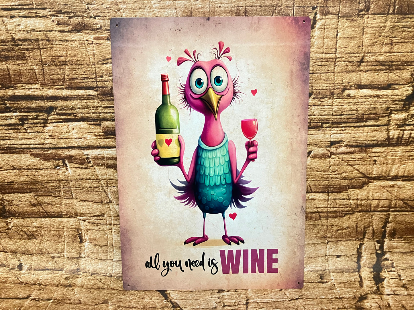 Humoristisch bord met een cartoonvogel met roze veren en een wijnfles en wijnglas in de vleugels, omringd door rode hartjes, met de tekst “all you need is WINE” op een rustieke houten achtergrond.