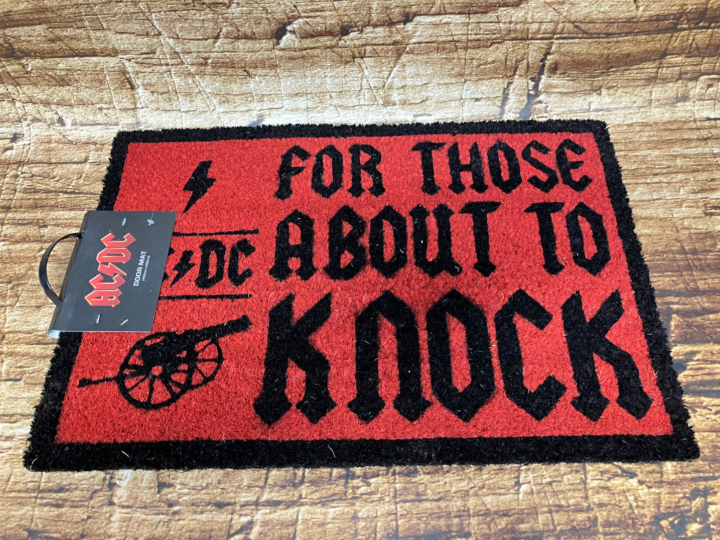 Rood‑zwarte AC/DC‑deurmat met de tekst “For Those About to Knock”, het bandlogo en een rock‑illustratie.