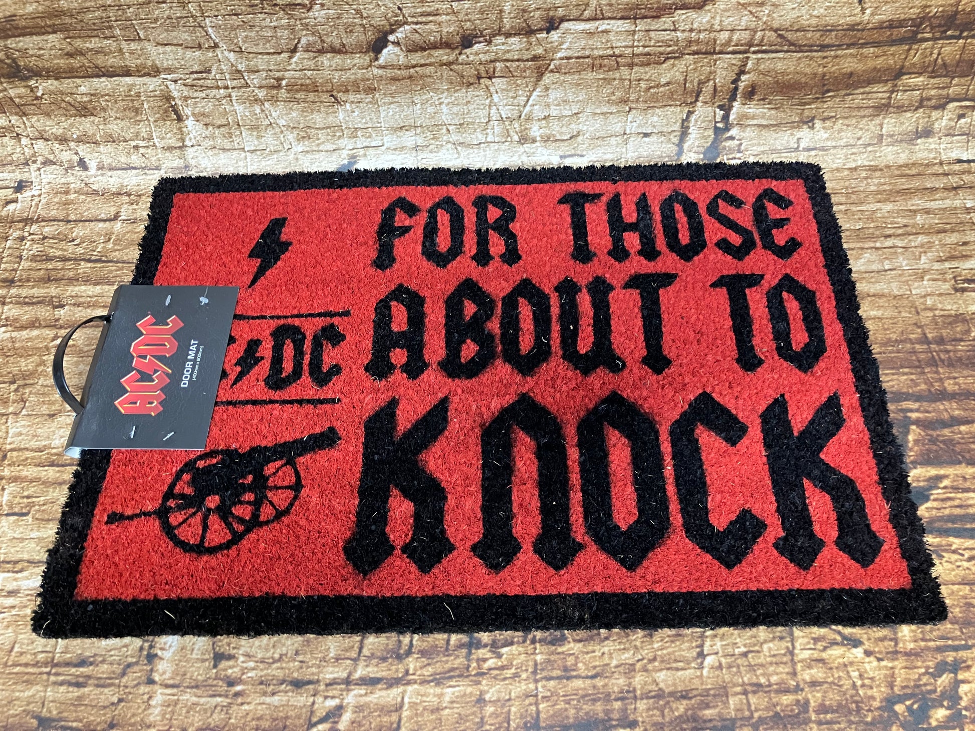 Rood‑zwarte AC/DC‑deurmat met de tekst “For Those About to Knock”, het bandlogo en een rock‑illustratie.