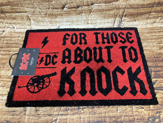 Rood‑zwarte AC/DC‑deurmat met de tekst “For Those About to Knock”, het bandlogo en een rock‑illustratie.