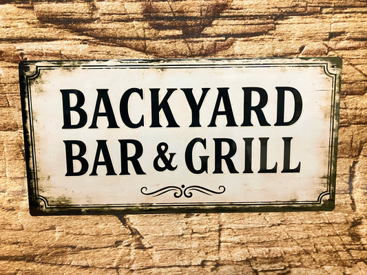 Decoratief bord met de tekst “Backyard Bar & Grill” in een vintage, verweerde stijl tegen een houten achtergrond.