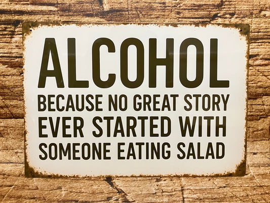 Vintage metalen bord met zwarte tekst “ALCOHOL – BECAUSE NO GREAT STORY EVER STARTED WITH SOMEONE EATING SALAD” op een witte, verweerde achtergrond, gemonteerd op hout voor een humoristische en informele uitstraling.