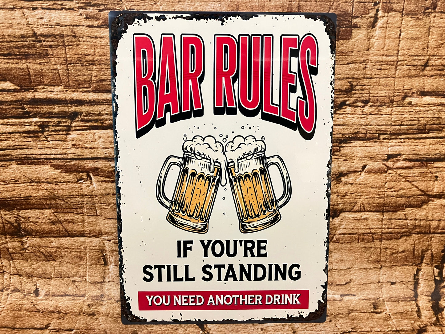 Humoristisch decoratief bord met twee proostende bierpullen en de tekst “BAR RULES – IF YOU'RE STILL STANDING YOU NEED ANOTHER DRINK”, op een houten achtergrond met vintage uitstraling.