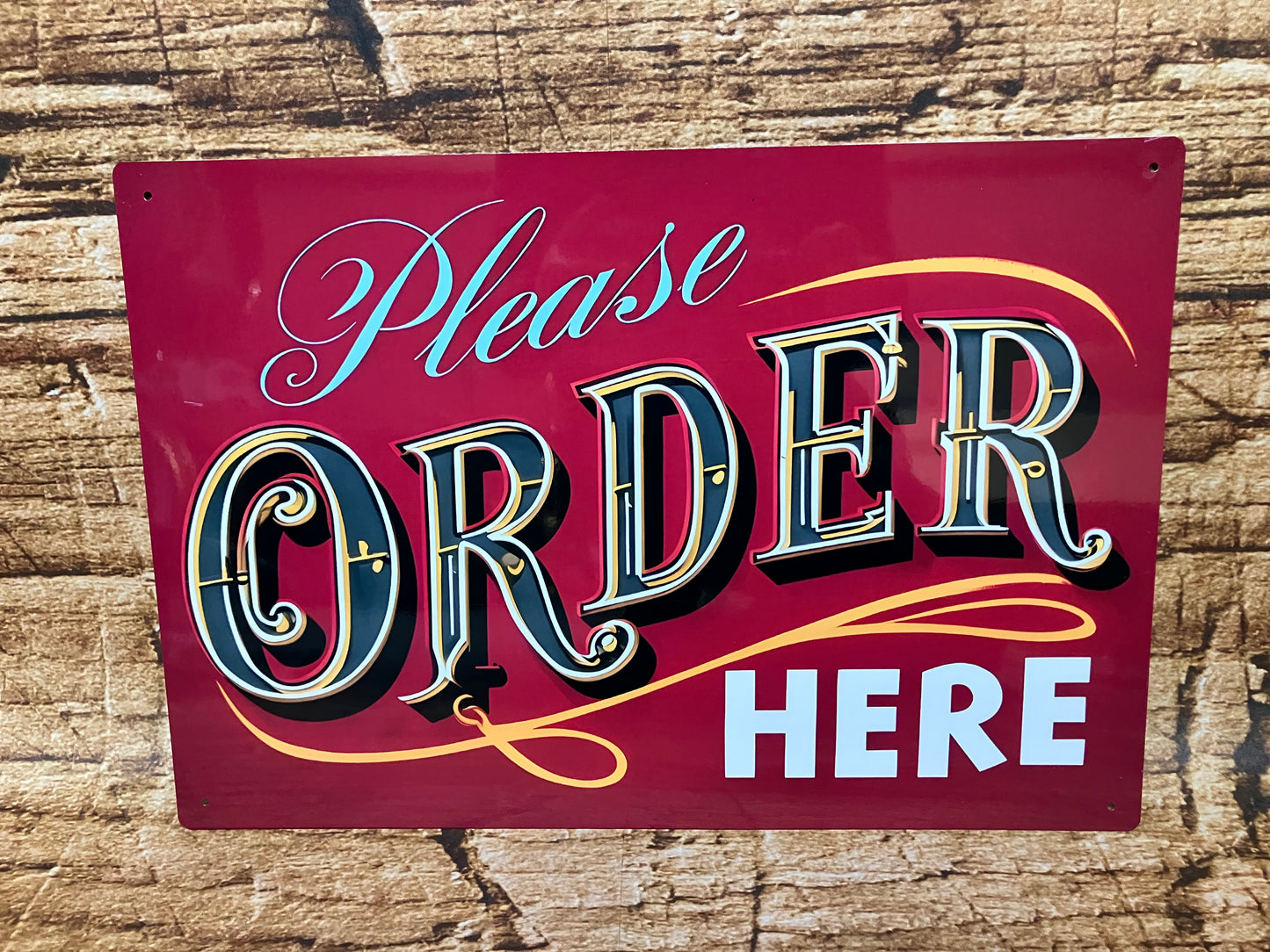 Decoratief bord met rode achtergrond en opvallende tekst “Please ORDER HERE”, waarbij “ORDER” groot en kleurrijk is vormgegeven in vintage stijl, gemonteerd op een houten oppervlak voor gebruik in horeca of foodservice.
