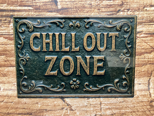 Decoratief bord met goudkleurige tekst “CHILL OUT ZONE” en sierlijke rand met bloemenmotief, op een donkere, verweerde achtergrond gemonteerd op hout, voor een rustgevende en stijlvolle uitstraling.