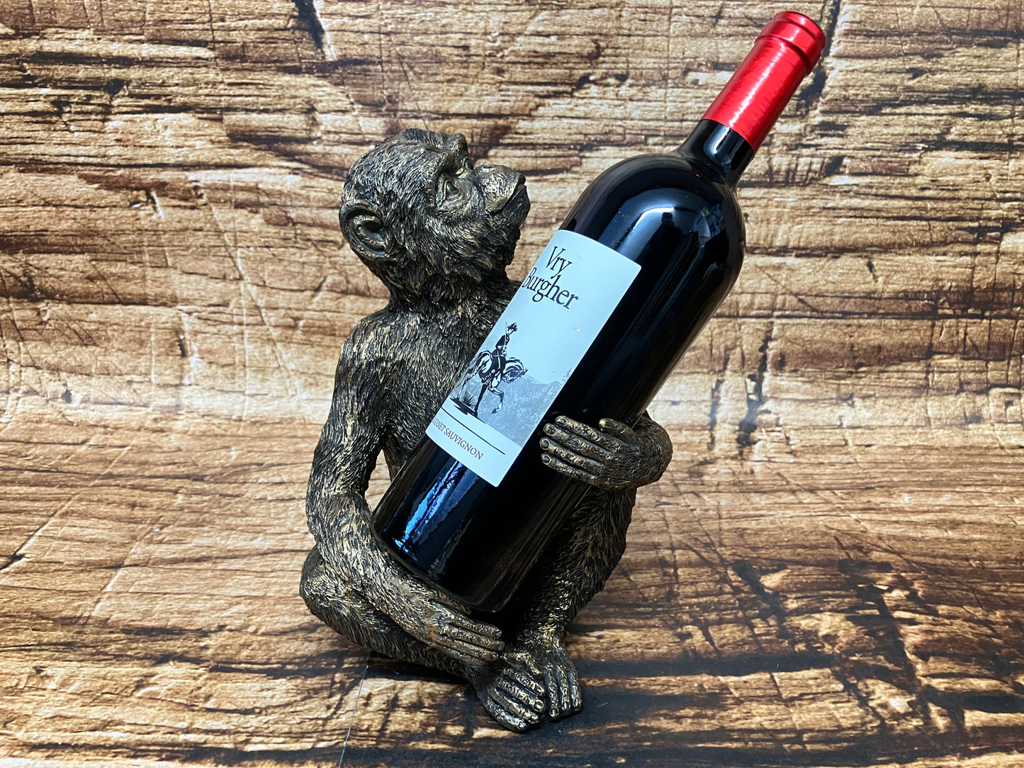 Decoratieve aap‑wijnfleshouder die een wijnfles omarmt, geplaatst op een houten oppervlak.