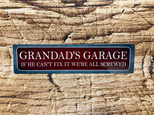  Humoristisch metalen bord met de tekst “GRANDAD'S GARAGE – IF HE CAN'T FIX IT WE'RE ALL SCREWED”, op een houten achtergrond, met een vintage rode kleur en metalen rand.
