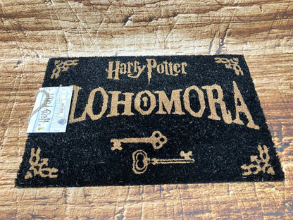 Zwarte Harry Potter‑deurmat met het woord “Alohomora” in goudkleurige letters, twee vintage sleutels en decoratieve hoeken.