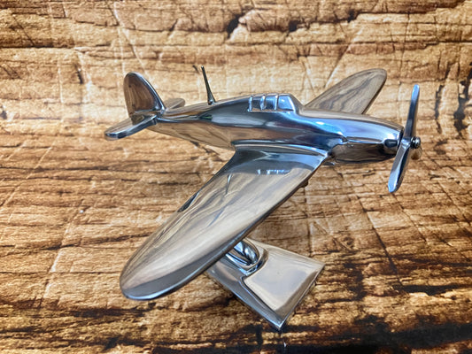 Gepolijst metalen model van een vintage propellervliegtuig met gestroomlijnde romp, frontale propeller en cockpitkap, gemonteerd op een standaard.