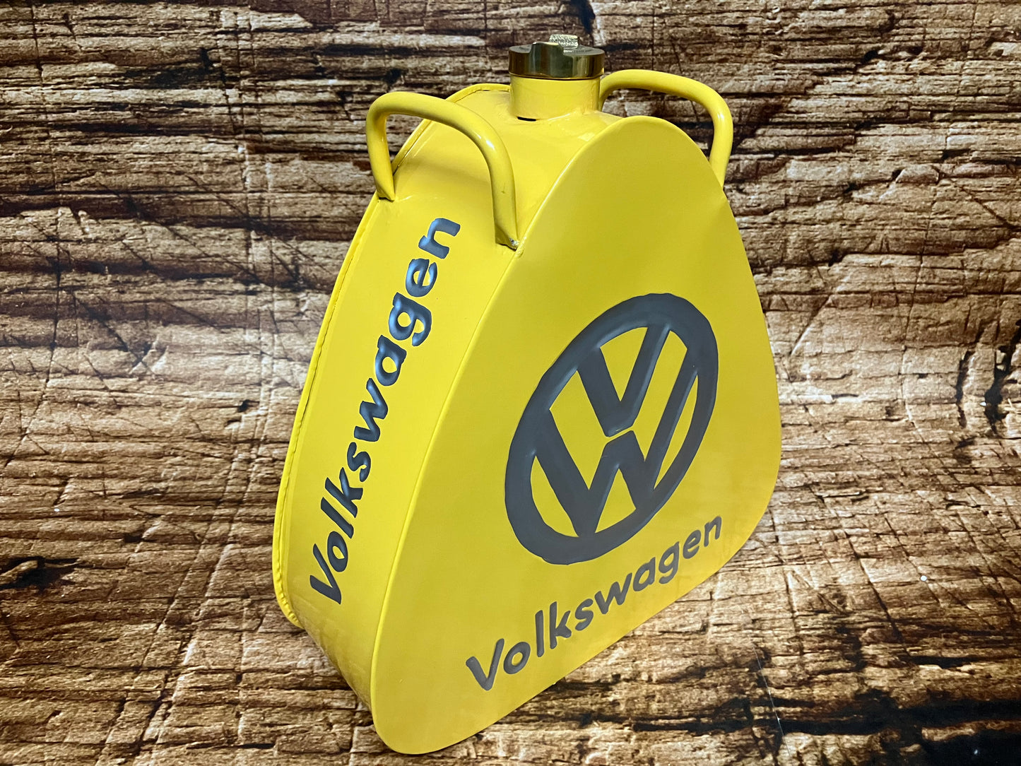 "Gele vintage Volkswagen metalen brandstof- of oliekannister met grijs VW‑logo, driehoekige vorm, messing dop en dubbele handgrepen, gebruikt als oldtimer- en garage‑decoratie."