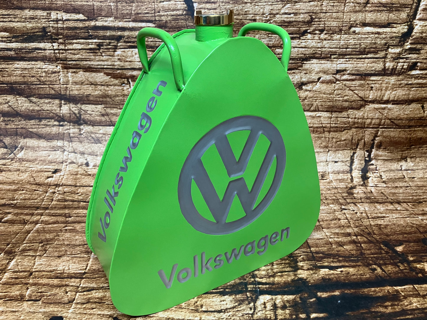 "Groene vintage Volkswagen metalen brandstof- of oliekannister met grijs VW‑logo, driehoekige vorm, messing dop en dubbele handgrepen, gebruikt als oldtimer- en garage‑decoratie."