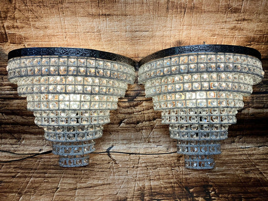 “Twee luxe kristallen wandlampen met donkere metalen rand en warm licht, gemonteerd tegen een houten achtergrond.”