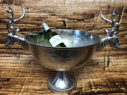 Luxe metalen wijnkoeler met twee gedetailleerde hertenkoppen als handgrepen, gevuld met ijs en een fles witte wijn, geplaatst op een houten ondergrond.