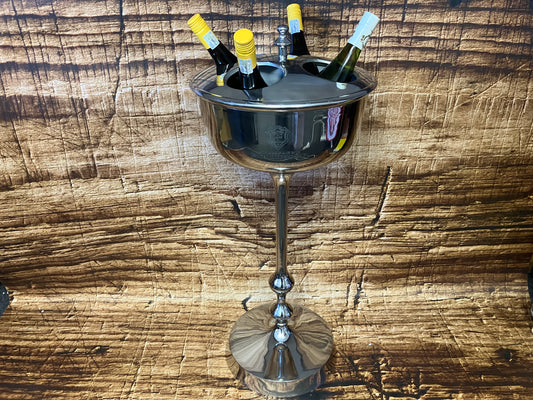 Luxe metalen wijnkoeler op een elegante standaard met meerdere wijnflessen rechtop in een ronde koeler met uitsparingen, geplaatst tegen een rustieke houten achtergrond.