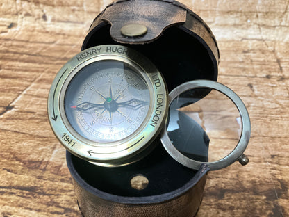   
"Een vintage messing kompas uit 1941, vervaardigd door Henry Hughes Ltd. in Londen, ligt open in een ronde leren etui op een houten ondergrond. De kompasroos toont duidelijke windrichtingen en gradenmarkeringen, terwijl een fijn naaldje naar het noorden wijst. De leren behuizing heeft een knoopsluiting en een kleine ingebouwde vergrootlens die boven het glas rust, wat het instrument een authentieke, historische uitstraling geeft. De warme tinten van het messing en het verweerde leer benadrukken het antie