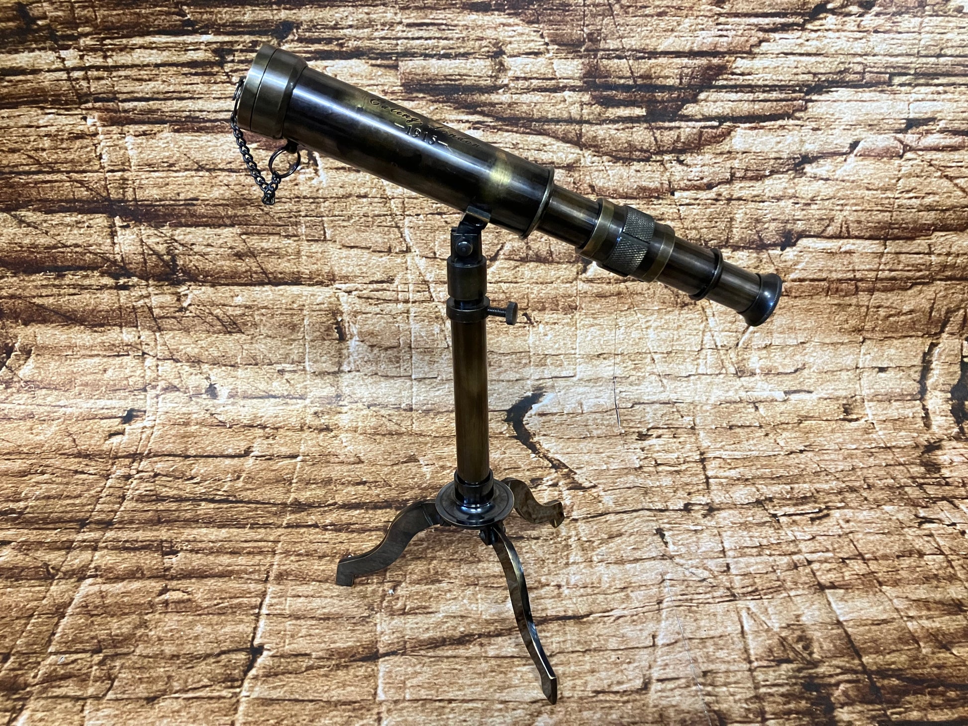 Vintage messing telescoop op een klein tripod‑statief, met meerdere uitschuifsegmenten en kettingdetail.
