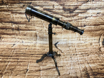 Vintage messing telescoop op een klein tripod‑statief, met meerdere uitschuifsegmenten en kettingdetail.