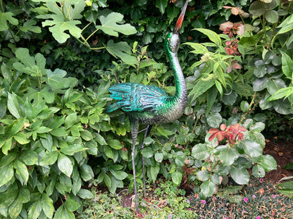 Metalen reiger sculptuur in blauw‑groene tinten, met gedetailleerde veren en slanke poten