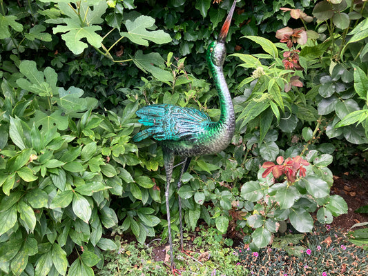 Metalen reiger sculptuur in blauw‑groene tinten, met gedetailleerde veren en slanke poten