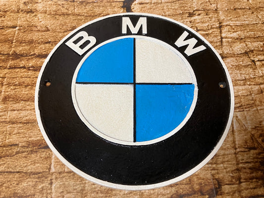 Rond metalen BMW embleem met zwart-wit-blauw logo op houten achtergrond, geschikt als decoratiebord.