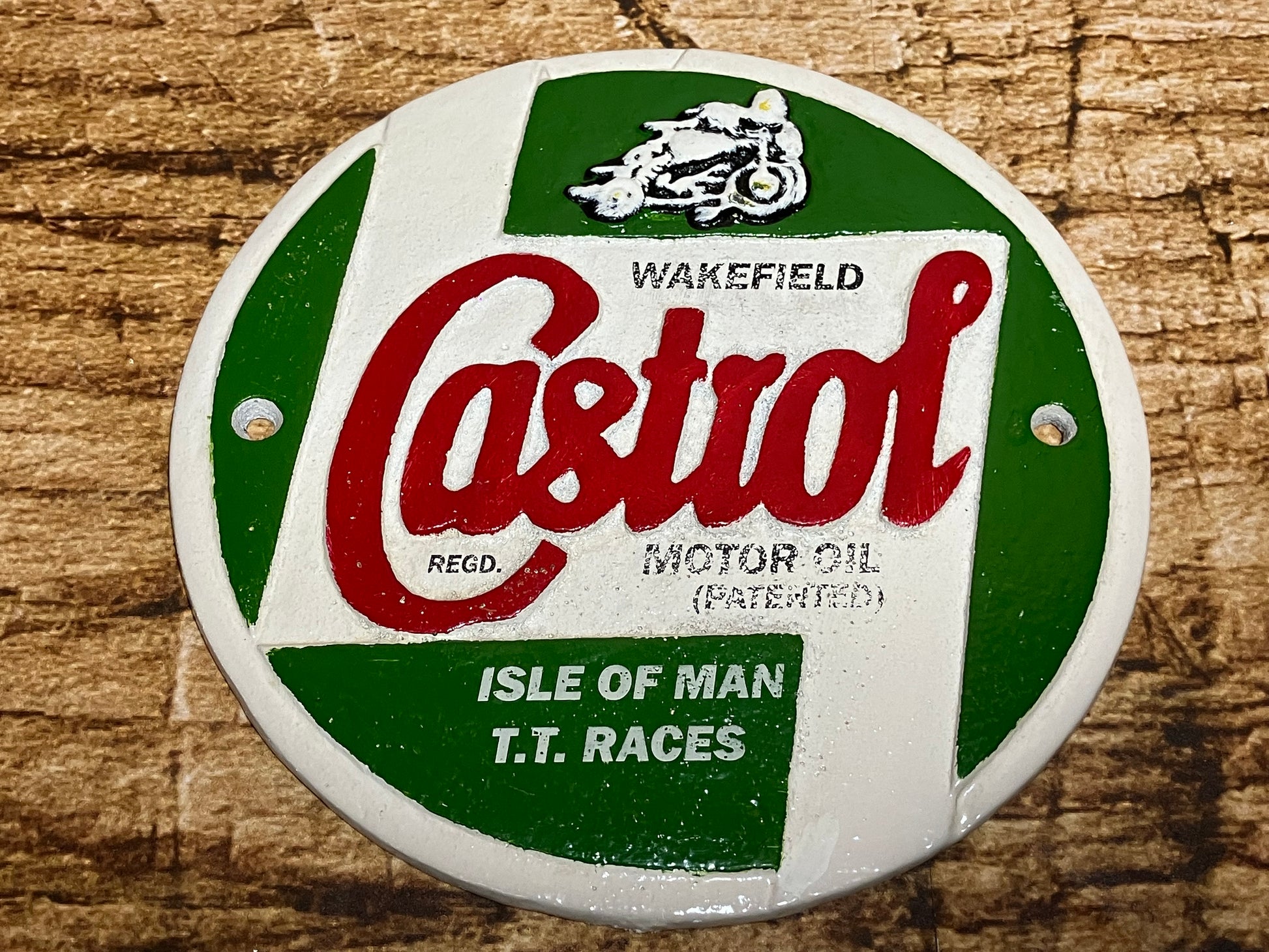 Ronde metalen Castrol‑plaat met groen‑wit ontwerp, rood Castrol‑logo en verwijzing naar Isle of Man TT‑races, geschikt als retro wanddecoratie voor garage of mancave.