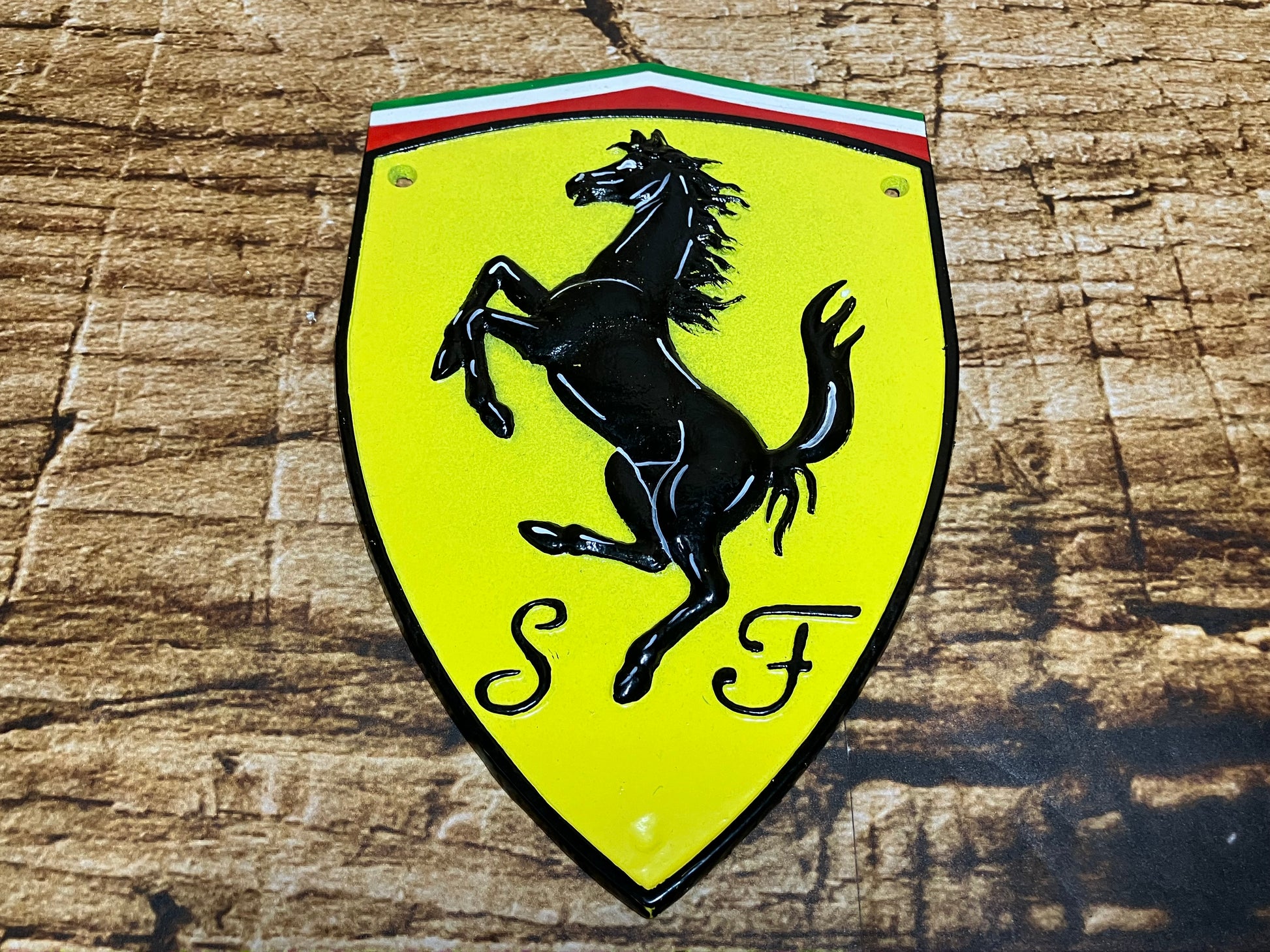 Metalen Ferrari‑schild met geel logo, zwart steigerend paard en Italiaanse vlagkleuren, ideaal als luxe wanddecoratie voor garage of mancave.