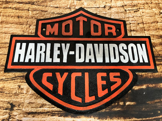 "Metalen wandplaat met het klassieke Harley‑Davidson Motor Cycles logo in zwart, wit en oranje 
