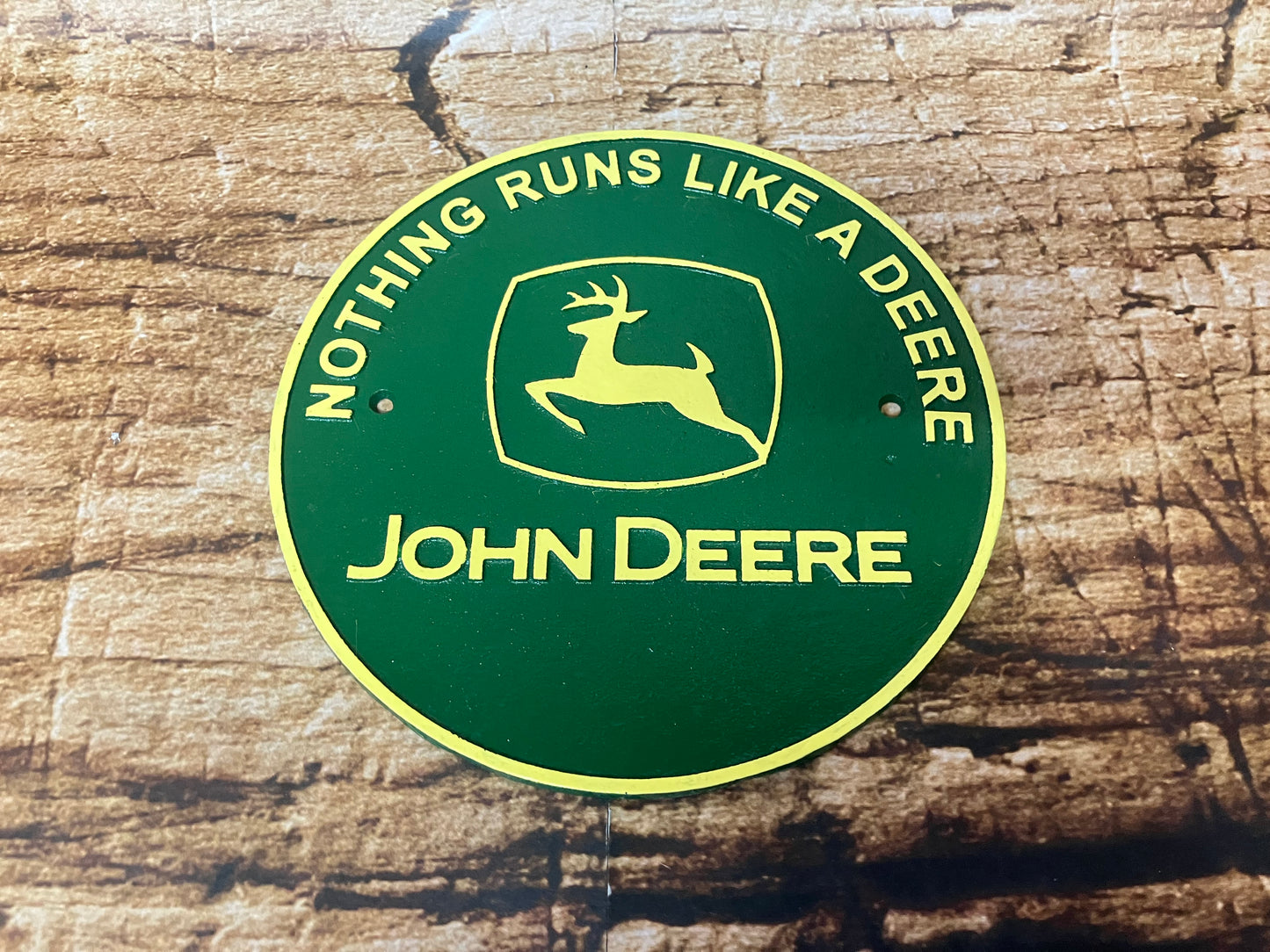 Rond metalen John Deere bord in groen en geel met springend hert‑logo en de tekst “Nothing Runs Like a Deere”, gebruikt als vintage tractor decoratie.