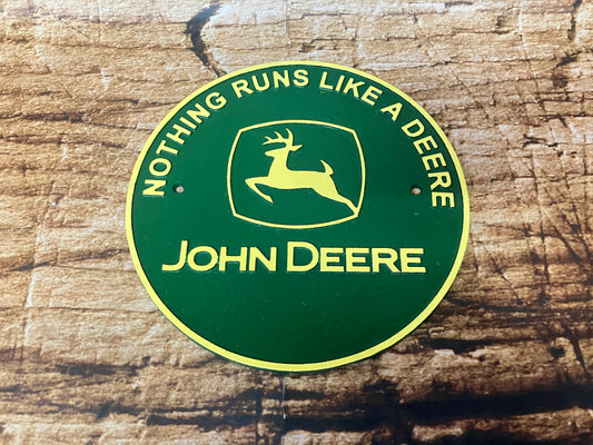Rond metalen John Deere bord in groen en geel met springend hert‑logo en de tekst “Nothing Runs Like a Deere”, gebruikt als vintage tractor decoratie.