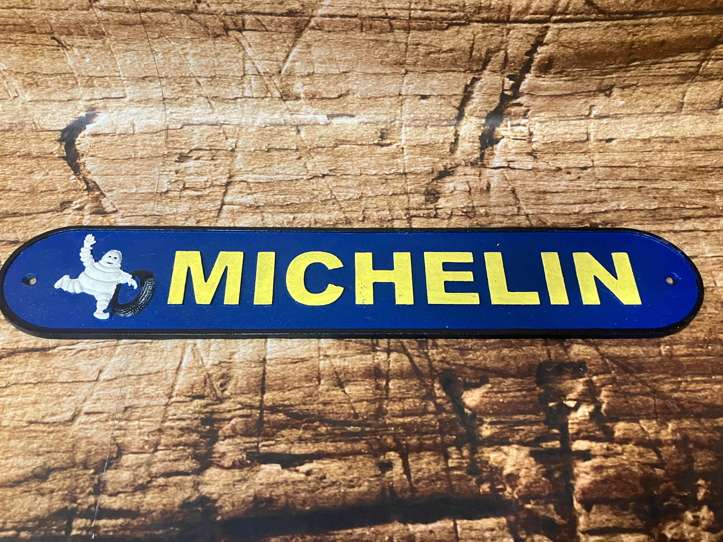Blauw metalen Michelin bord met de Michelin Man en geel logo, gebruikt als vintage garage decoratie.