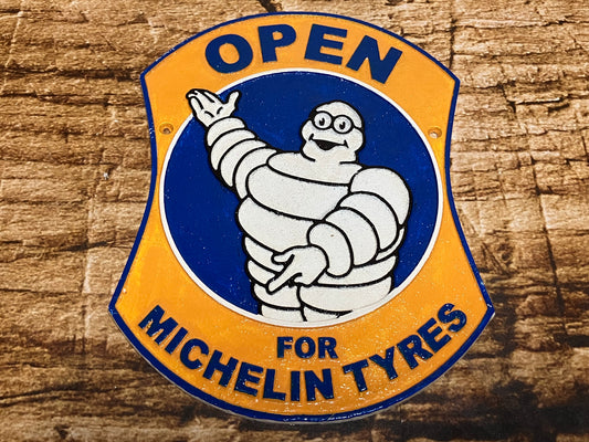 Vintage metalen Michelin‑bord met de Michelin Man (Bibendum) in blauw‑gele stijl en de tekst “Open for Michelin Tyres”, geschikt als retro wanddecoratie voor garage of mancave.