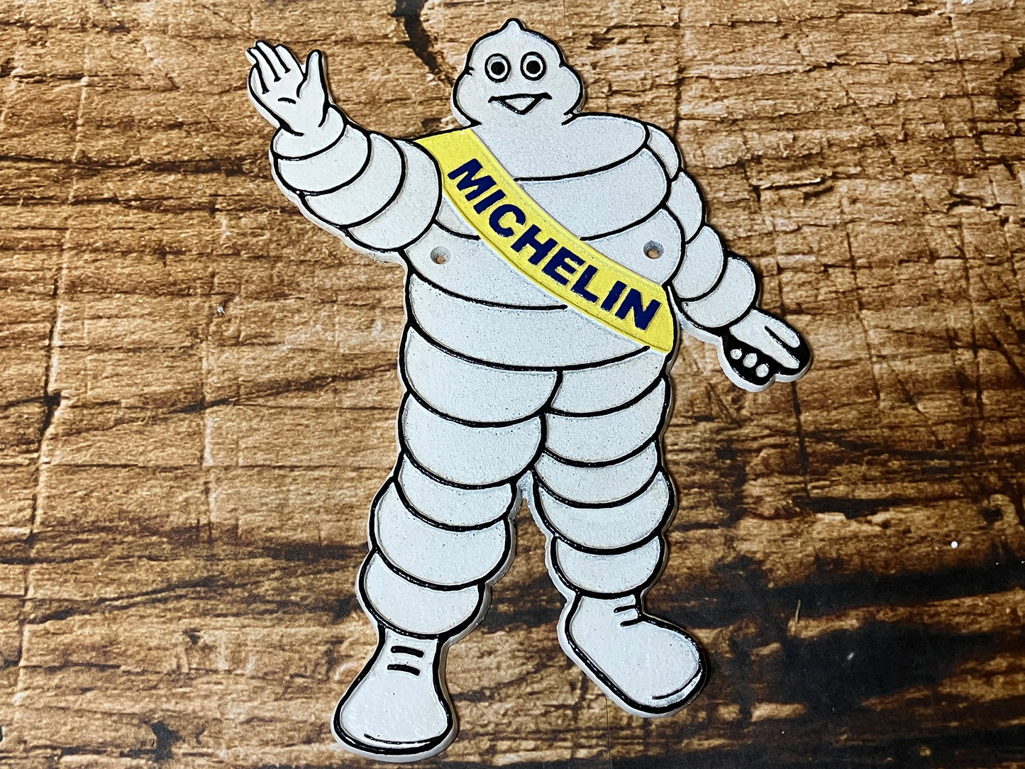 Gietijzeren Michelin bord met Bibendum en gele Michelin‑sjerp, gebruikt als vintage garage‑ en mancave decoratie.