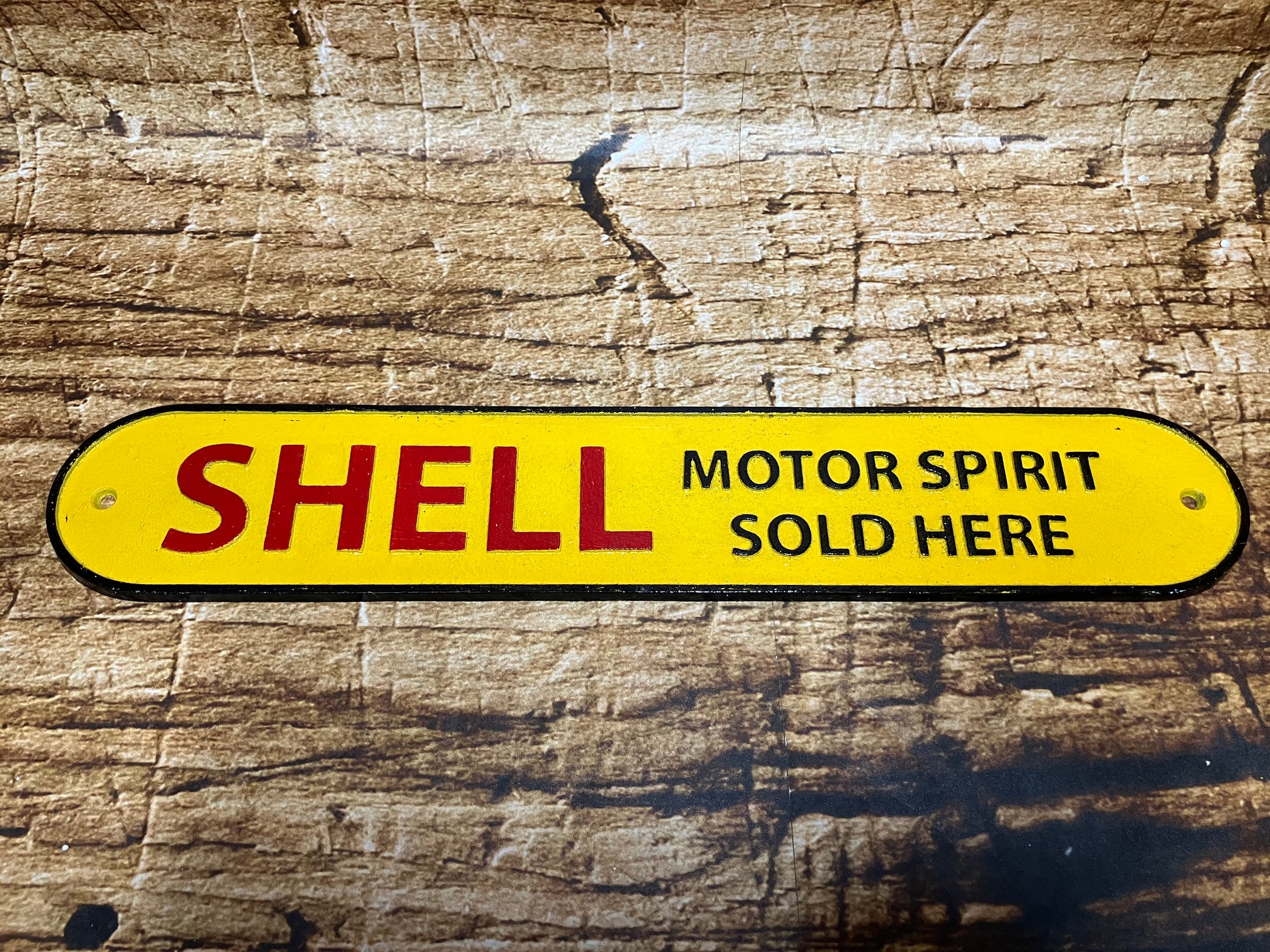 Gietijzeren Shell bord met gele achtergrond en de tekst “Shell Motor Spirit Sold Here”, gebruikt als vintage garage‑ en mancave decoratie.