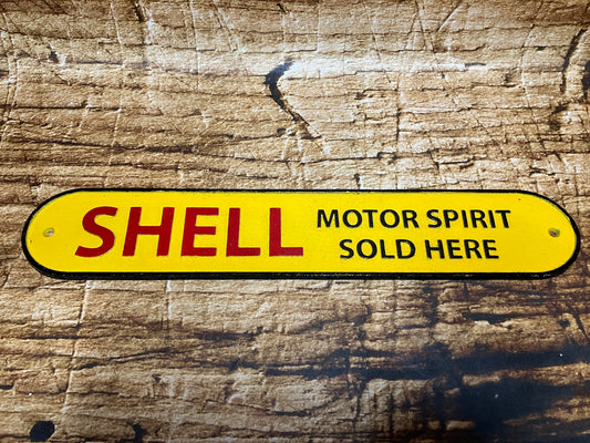 Gietijzeren Shell bord met gele achtergrond en de tekst “Shell Motor Spirit Sold Here”, gebruikt als vintage garage‑ en mancave decoratie.