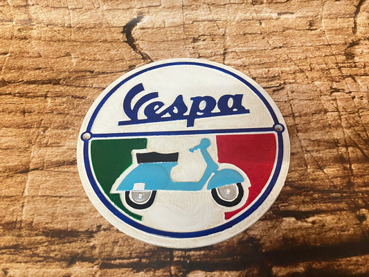 Rond metalen Vespa bord met blauwe scooter en Italiaanse vlagkleuren, gebruikt als retro scooterdecoratie.