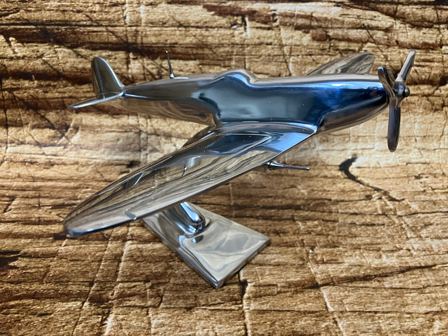 Gepolijst metalen model van een vintage propellervliegtuig met gestroomlijnde romp en frontale propeller, gemonteerd op een standaard.