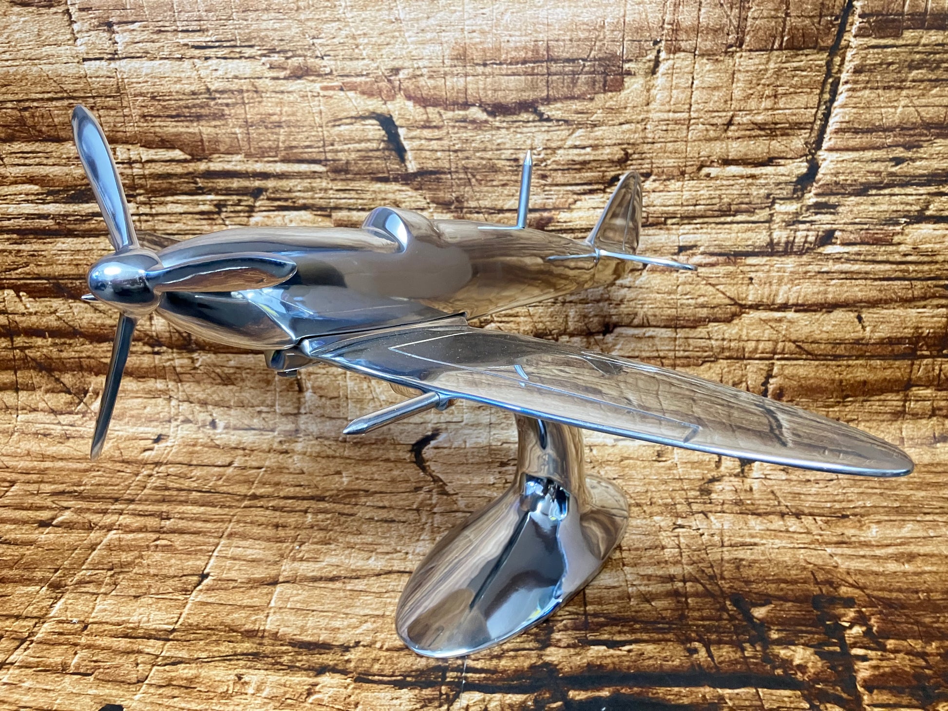 "Aluminium vliegtuigmodel op een gebogen standaard, gefotografeerd op een houten ondergrond; decoratief object met vintage jachtvliegtuig‑design."