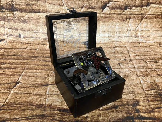 "Vintage zonnewijzer‑kompas in zwarte box met metalen frame, Romeinse cijfers en ingebouwd kompas, gebruikt als decoratief en verzamelobject."