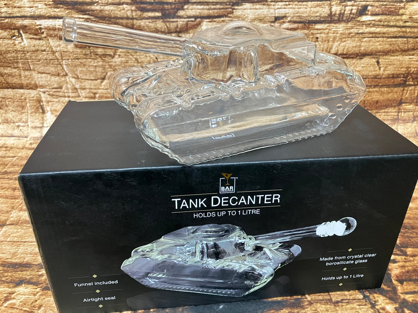   
"Een transparante glazen decanter in de vorm van een gedetailleerde militaire tank staat boven op een zwarte doos. De decanter heeft zorgvuldig uitgewerkte elementen zoals een draaibare koepel, een lange loop en realistisch vormgegeven rupsbanden, allemaal volledig van glas. Het glas vangt het licht waardoor subtiele reflecties ontstaan.  De presentatie oogt luxe en bedoeld als opvallend baraccessoire of cadeau.