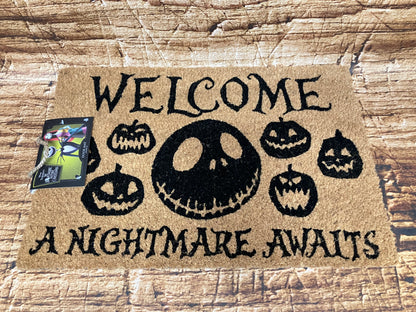 Beige Halloween‑deurmat met groot Jack‑gezicht en de tekst “Welcome – A Nightmare Awaits”, omringd door kleine pompoengezichten.