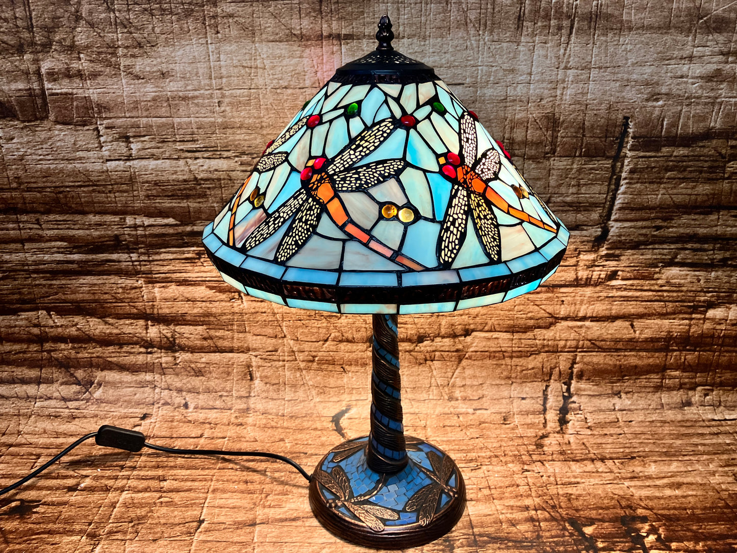 Tiffany-stijl tafellamp met blauwkleurige glazen kap, versierd met libellen met gele en zwarte vleugels en kleurrijke glaskralen; decoratieve voet met bijpassend motief en gedraaide steel en verlicht voor warme gloed.