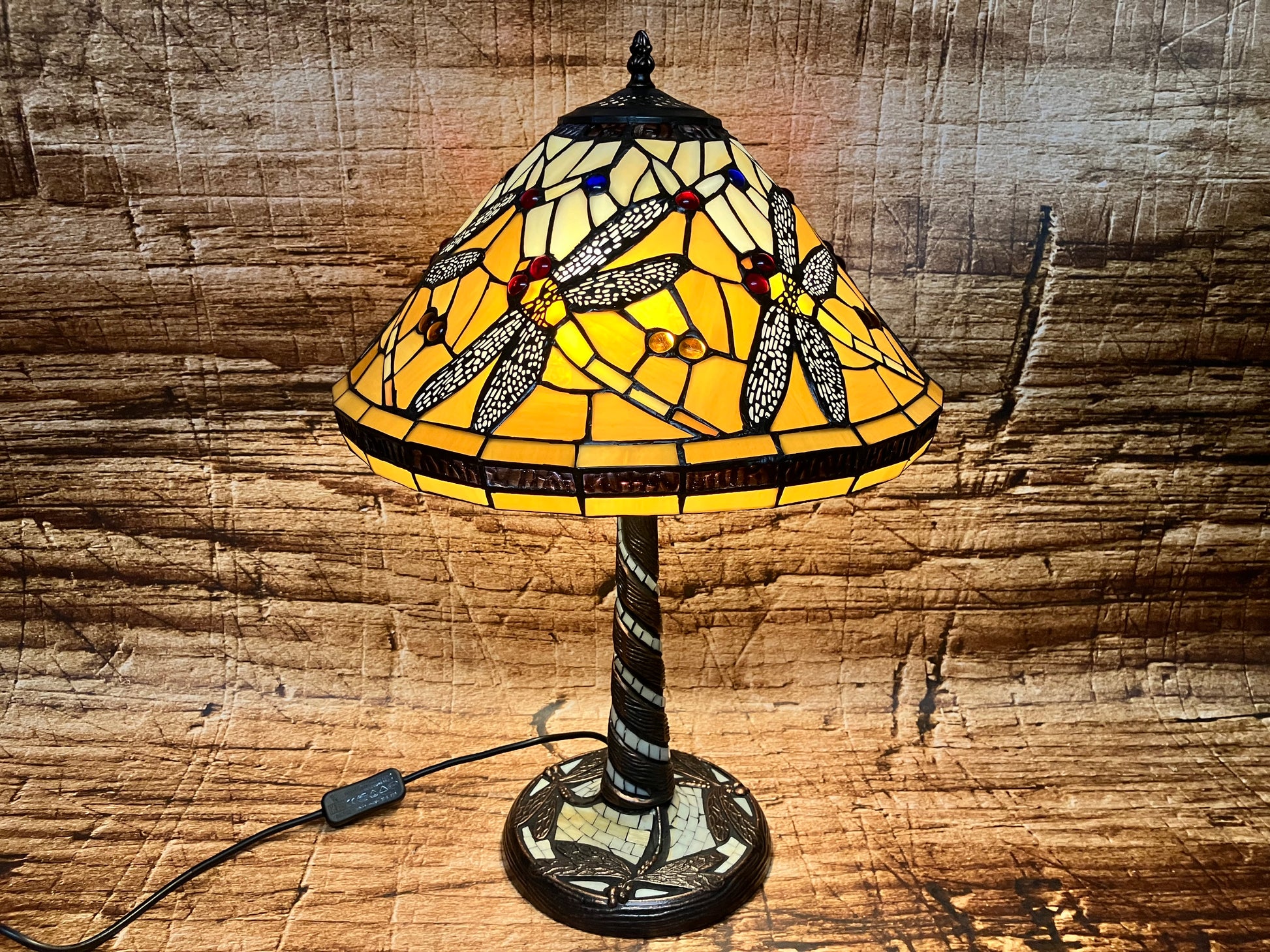 Tiffany-stijl tafellamp met amberkleurige glazen kap, versierd met libellen met gedetailleerde vleugels en kleurrijke glazen accenten; decoratieve voet met bijpassend glasontwerp en verlicht voor warme gloed.