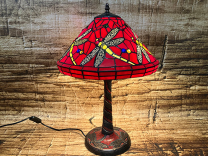 Tafellamp met roodkleurige glazen kap in Tiffany-stijl, versierd met libellen met gele en zwarte vleugels en kleurrijke glaskralen; decoratieve voet met gedraaid ontwerp.
