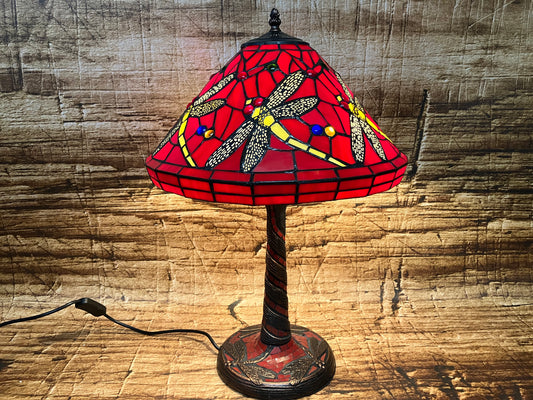 Tafellamp met roodkleurige glazen kap in Tiffany-stijl, versierd met libellen met gele en zwarte vleugels en kleurrijke glaskralen; decoratieve voet met gedraaid ontwerp.