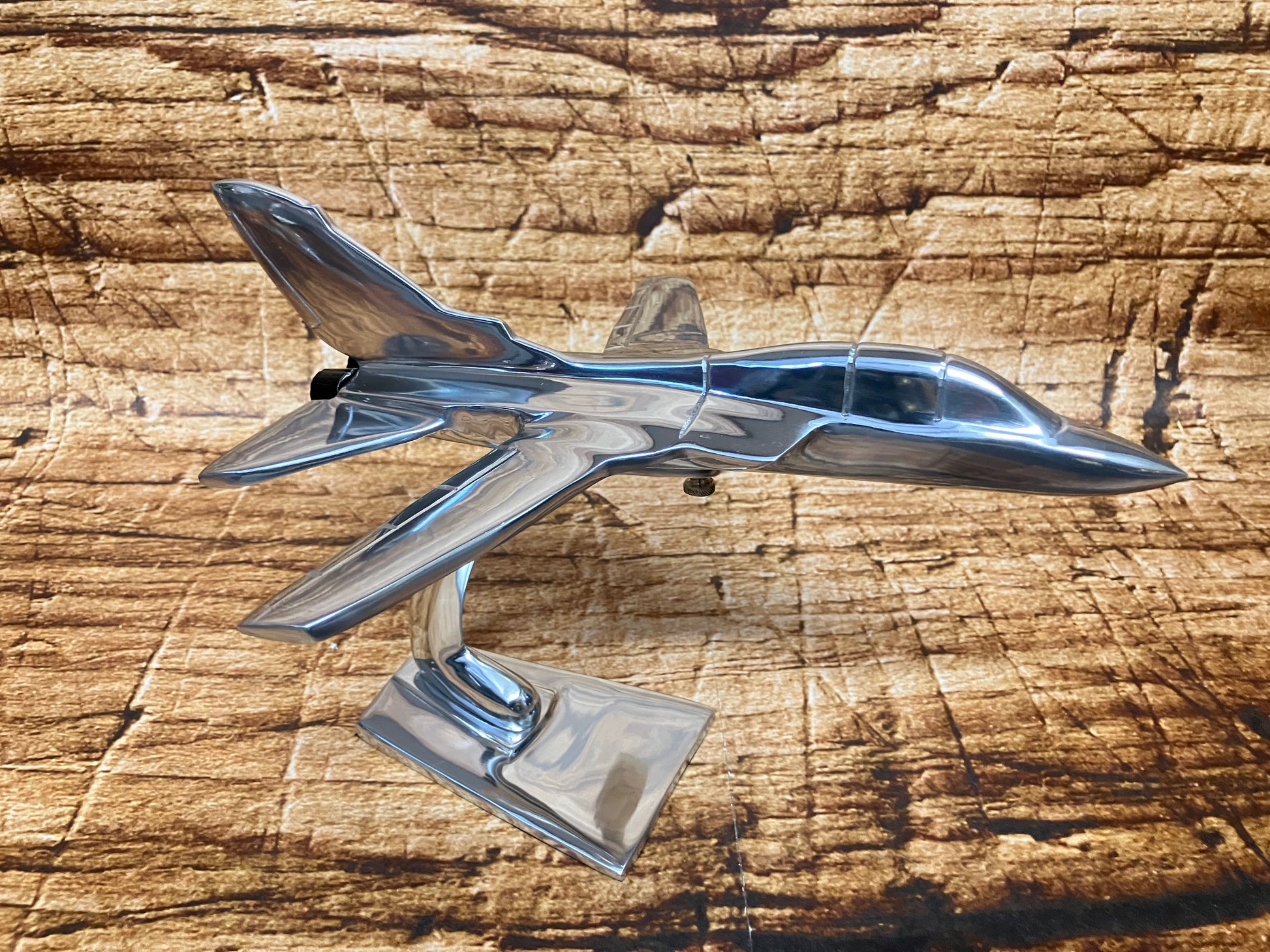 Gepolijst metalen model van een straalvliegtuig met gedetailleerde vleugels, staartvinnen en cockpitramen, gemonteerd op een standaard.