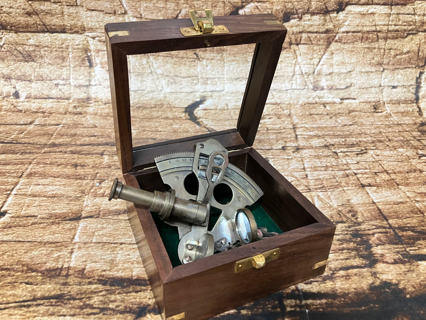 "Vintage nautische sextant in houten box met glasplaat, metalen onderdelen en groene viltvoering, gebruikt als decoratief en verzamelobject."
