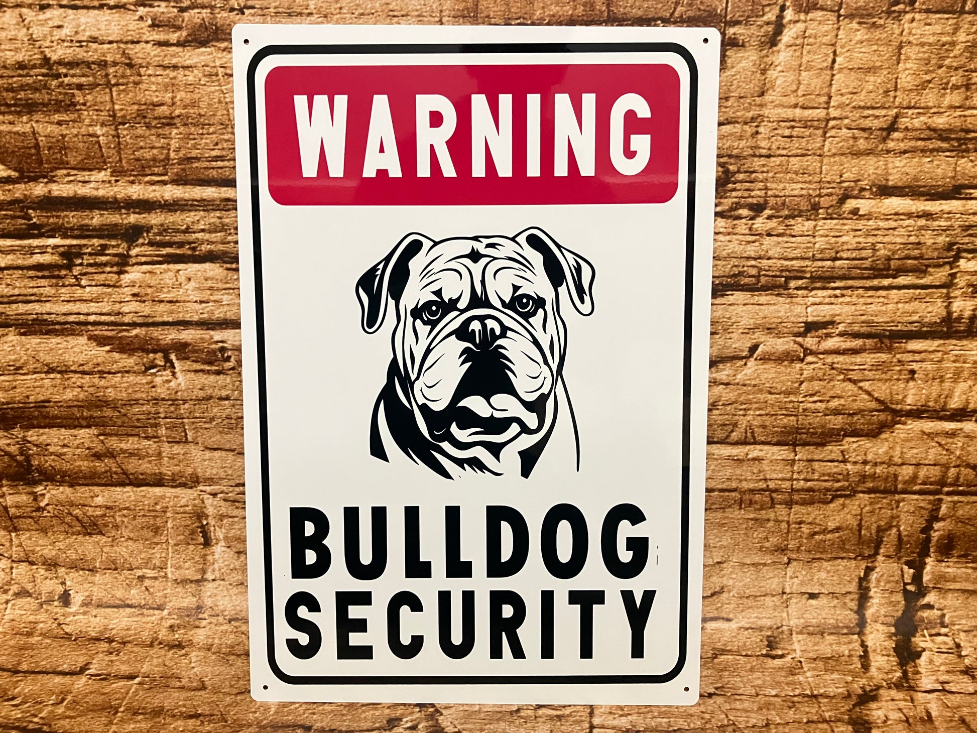 Waarschuwingsbord met een rode kopregel met het woord “Warning”, daaronder een zwart‑wit illustratie van een bulldog met een stoere, alerte blik. Onder de afbeelding staat in grote zwarte hoofdletters “Bulldog Security”. Het bord heeft een zwarte rand en hangt tegen een houten achtergrond, waardoor het geheel een robuuste, licht humoristische beveiligingsuitstraling krijgt.