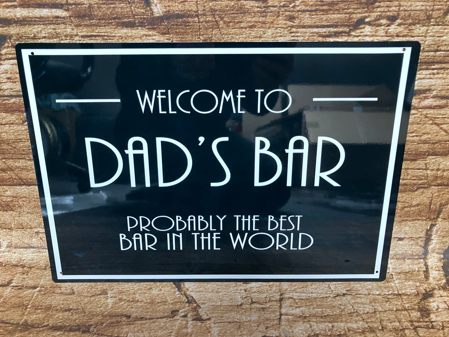 Decoratief bord met witte tekst “Welcome to Dad’s Bar – Probably the best bar in the world” op zwarte achtergrond met witte rand, gemonteerd op hout voor een gezellige en humoristische sfeer.