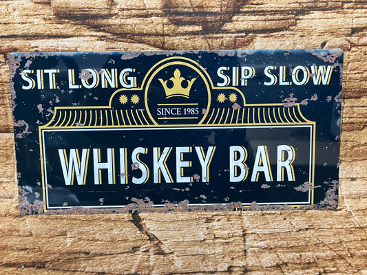 Vintage metalen bord met de tekst “SIT LONG SIP SLOW – SINCE 1985 – WHISKEY BAR”, in sierlijke letters met kroonembleem en decoratieve lijnen, op een verweerde houten achtergrond voor een klassieke baruitstraling.